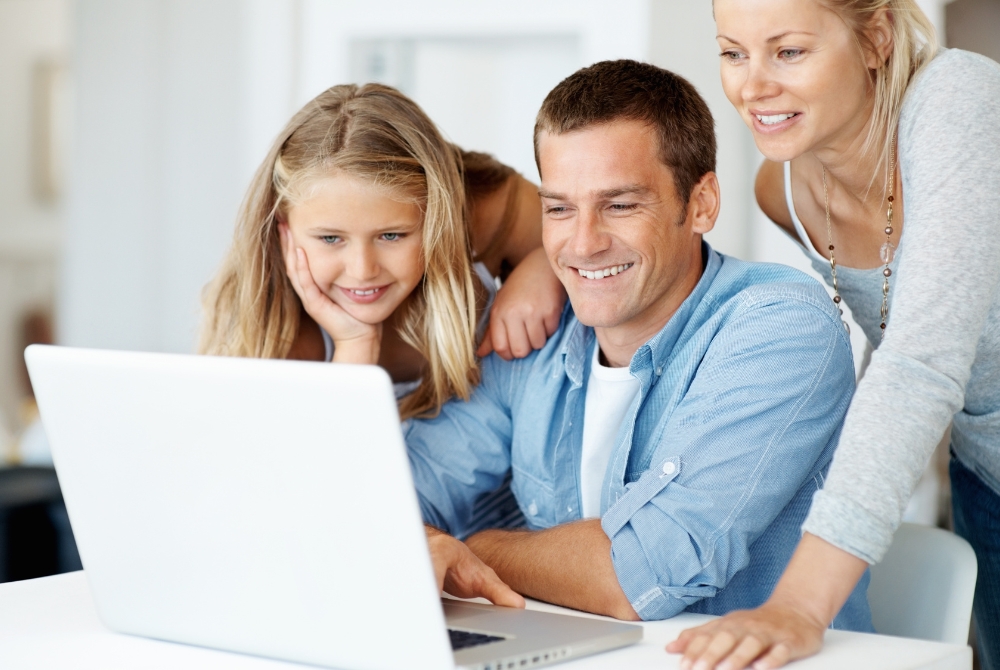 image of a husband and wife with daughter at the kitchen table looking at a whats on the laptop